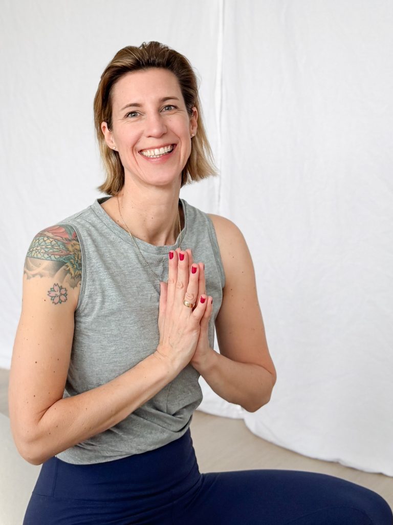 Eine Frau hält ihre Hände vors Herz, macht den Yogagruß und lacht in die Kamera