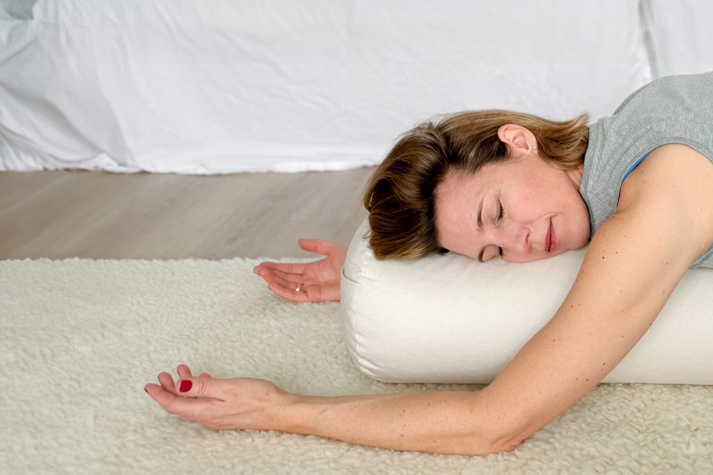 Eine Frau macht Yin Yoga, sie liegt mit geschlossenen Augen auf einem Bolster