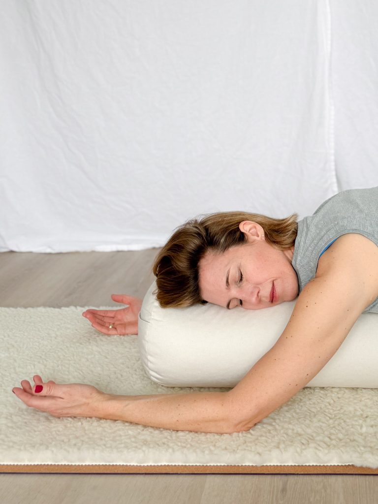 Eine Frau macht Yin Yoga, sie liegt mit geschlossenen Augen auf einem Bolster